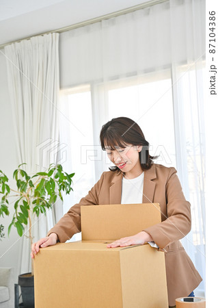 机の上に置いた段ボールにモノを詰めて蓋をする女性 87104386