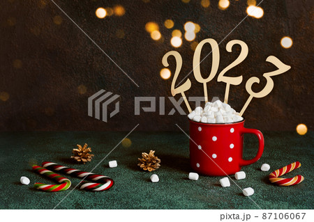 Christmas or New Year 2023 concept. Red mug with hot chocolate and marshmallows and golden numbers 2022, copy space 87106067