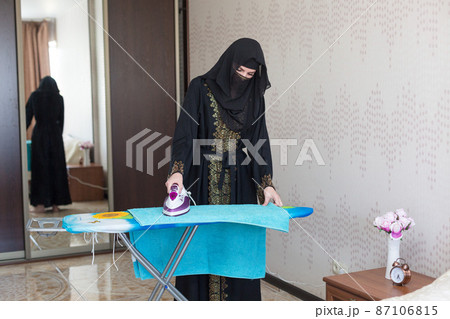 A Muslim woman in national clothes is doing household chores ironing a towel A Muslim woman in national clothes is doing household chores ironing a towel 87106815