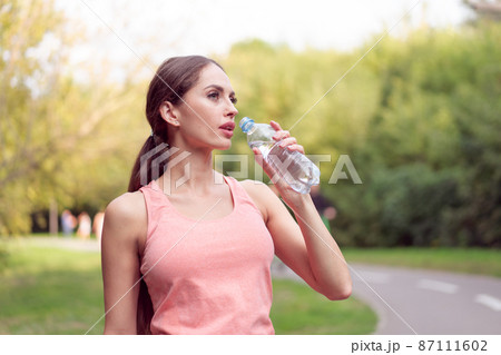 Athletic woman standing running track in summer park drink water after running exercises 87111602