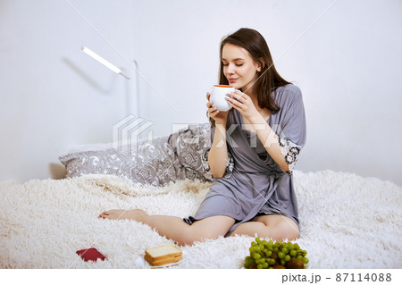 Breakfast in bed by young white woman with cup of coffee in hands. Breakfast in bed by young white woman with cup of coffee in hands. 87114088