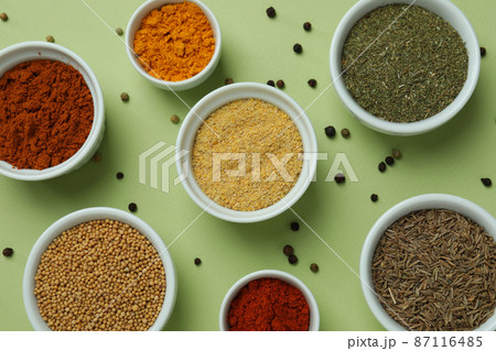 Set of different spices in bowls on green background Set of different spices in bowls on green background 87116485