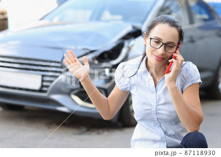 Woman driver is talking on phone in front of broken car Woman driver is talking on phone in front of broken car 87118930