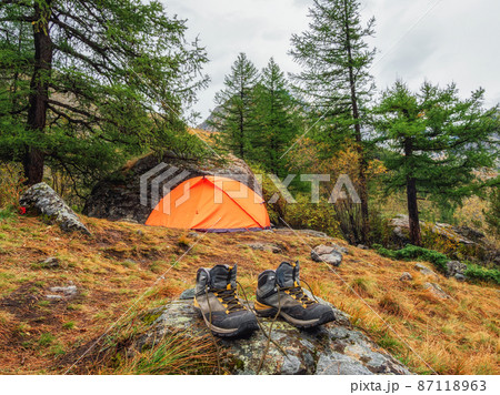 Wet hiking boots to dry. Atmospheric mountain landscape with tent under tree on hill in autumn colors in dense fog. Wet hiking boots to dry. Atmospheric mountain landscape with tent under tree on hill in autumn colors in dense fog. 87118963