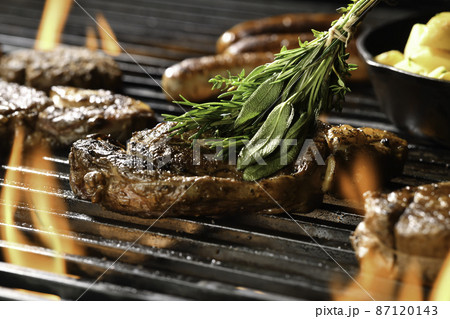 Cooked juicy steak meat beef brushed with rosemary on a flaming grill surrounded by other meat Cooked juicy steak meat beef brushed with rosemary on a flaming grill surrounded by other meat 87120143