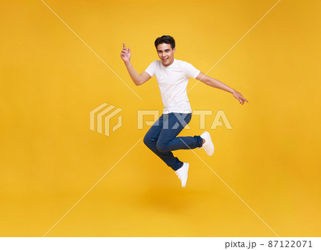 Happy Asian man smiling and jumping while celebrating success isolated over yellow background. 87122071