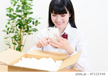 緩衝材の入った段ボール荷物を入れスマホを操作する女子高校生　宅配配送　通販　フリマアプリオークション 87122540