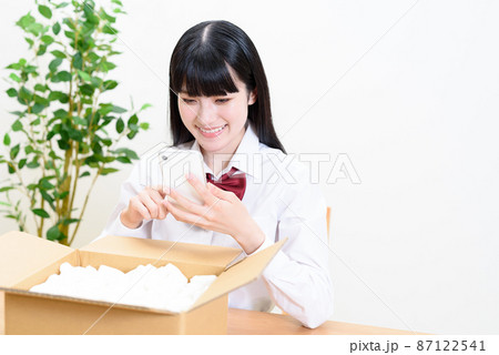 緩衝材の入った段ボール荷物を入れスマホを操作する女子高校生　宅配配送　通販　フリマアプリオークション 87122541