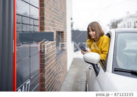 Woman opens post terminal cell using smart phone right out of the car window Woman opens post terminal cell using smart phone right out of the car window 87123235