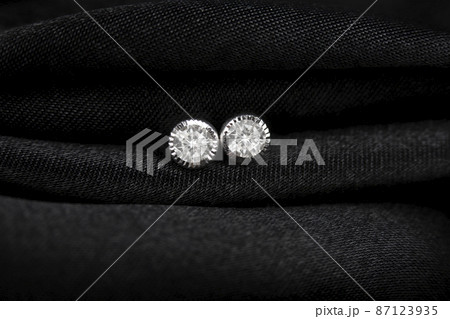 Round silver stud earrings with diamond on black fabric background. 87123935