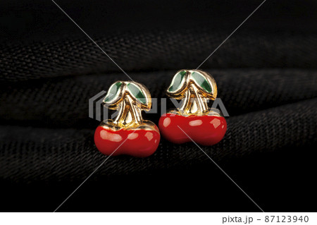 Cherry-shaped gold stud earrings on black fabric background. 87123940