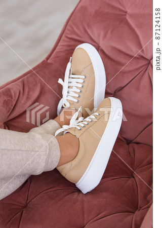 photo of a women legs in beige sports suit and stylish leather sneakers posing in the chair. selective focus photo of a women legs in beige sports suit and stylish leather sneakers posing in the chair. selective focus 87124158