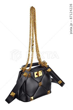 Miniature handbag made of genuine black leather with chains and pyramidal rivets made of golden metal, with a metal clasp isolated on a white background. Expensive women's accessories. 87124226