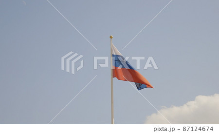 Russian flag on the flagpole waving in the wind against a blue sky with clouds Russian flag on the flagpole waving in the wind against a blue sky with clouds 87124674