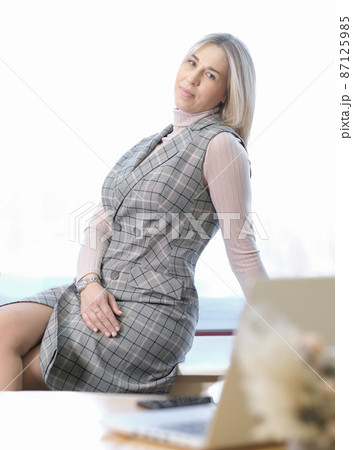 business woman having a break working indoors at office. beautiful blond woman employee sitting on a desk and getting rest. vertical shot. 87125985
