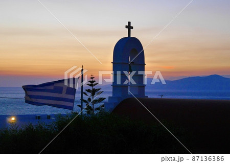 教会が佇みギリシャ国旗がたなびくミコノス島の夕景 87136386