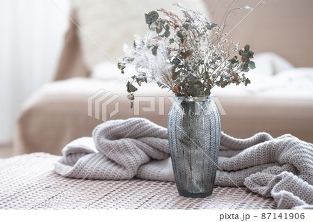 Home composition with a glass vase with dried flowers on a blurred background. Home composition with a glass vase with dried flowers on a blurred background. 87141906