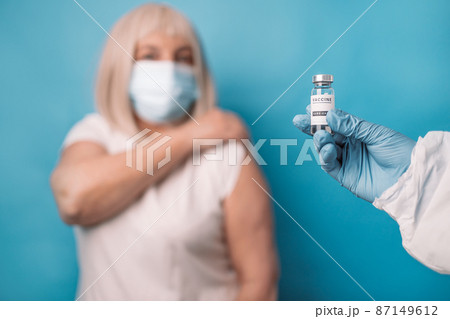 Doctor makes vaccination to senior woman, wearing face mask over blue background. 87149612