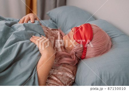 Positive relaxed 50s woman lying in bed with sleeping mask on a gray bed during lzy weekend Positive relaxed 50s woman lying in bed with sleeping mask on a gray bed during lzy weekend 87150010