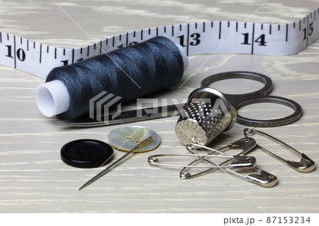 Supplies and equipment for sewing on a wood work surface cotton tape measure scissors thimble needle pins buttons 87153234