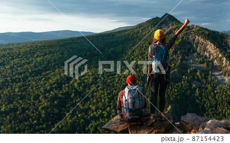 A traveling couple in hiking gear in the mountains at sunset. Two tourists on the top of the mountain. A man and a woman in the mountains. Hiking in the mountains with backpacks. Two travelers A traveling couple in hiking gear in the mountains at sunset. Two tourists on the top of the mountain. A man and a woman in the mountains. Hiking in the mountains with backpacks. Two travelers 87154423