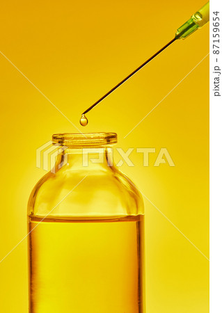 A drop of liquid drips from the needle of a medical syringe into the bottle. Front view. Macro photo. 87159654
