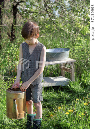 village boy in retro clothes with an iron watering can in the garden 87159998