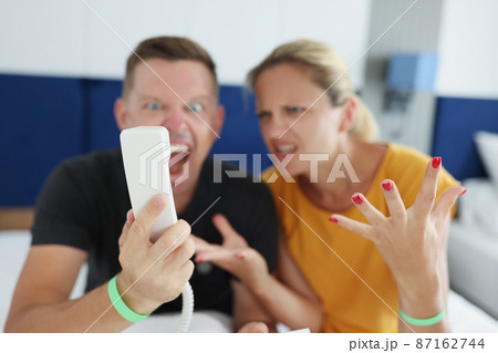 Couple yelling into phone while sitting on the bed in the hotel 87162744