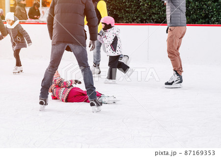 Soft,Selective focus.People, friendship, sport and leisure concept - happy friends on skating rink.Group of teenage friends ice skating on an ice rink.A kid takes relax after his fall while skating. 87169353