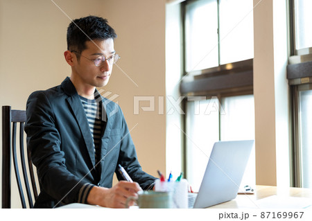 パソコン内のデータを見て新たに思い浮かんだインスピレーションを手帳に書き込もうとする起業家 87169967