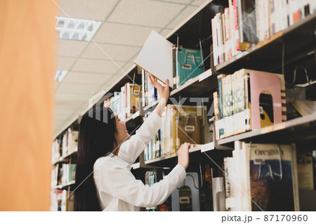Young Asian women are searching for books and reading books on the tables and aisles of the college libraries to research and develop their academic and education self Young Asian women are searching for books and reading books on the tables and aisles of the college libraries to research and develop their academic and education self 87170960