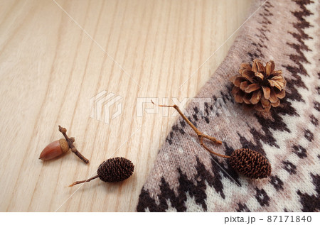 木のテーブルの上にニットと松ぼっくりとドングリとオオバヤシャブシ 87171840