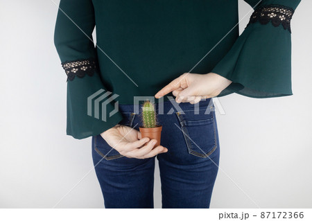 Concept. A woman holds a cactus as a symbol of rectal pain. Varicose veins of the lower intestine. Pain in the rectum, hemorrhoids and pain in the excretory system of the body. Proctology 87172366