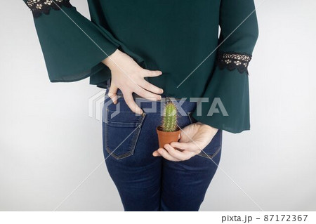 Concept. A woman holds a cactus as a symbol of rectal pain. Varicose veins of the lower intestine. Pain in the rectum, hemorrhoids and pain in the excretory system of the body. Proctology 87172367