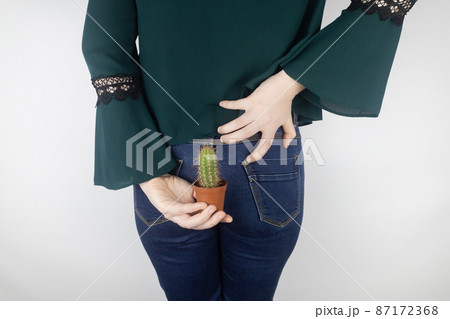 Concept. A woman holds a cactus as a symbol of rectal pain. Varicose veins of the lower intestine. Pain in the rectum, hemorrhoids and pain in the excretory system of the body. Proctology 87172368
