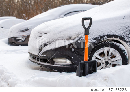 plastic snow shovel in front of snow-covered car at sunny winter morning 87173228