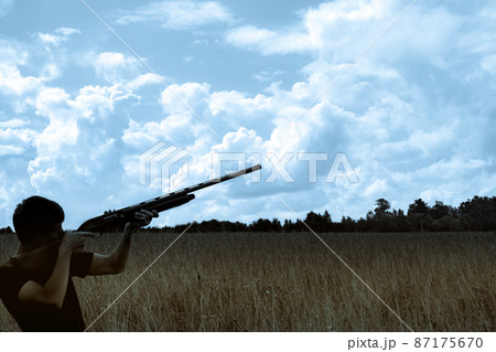 Young man hunter silhouette takes aim at a distant target blue sky yellow field 87175670