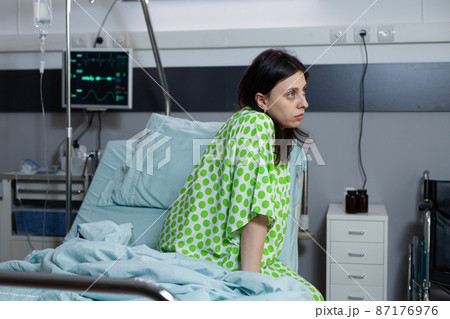 Patient with illness feeling depressed sitting on bedside looking into distance 87176976