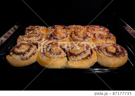 Twelve baked cinnamon buns on tray in electric oven at home Twelve baked cinnamon buns on tray in electric oven at home 87177735