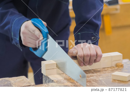 Man carpenter using hand saw to cutting wood on workbench - close up 87177821