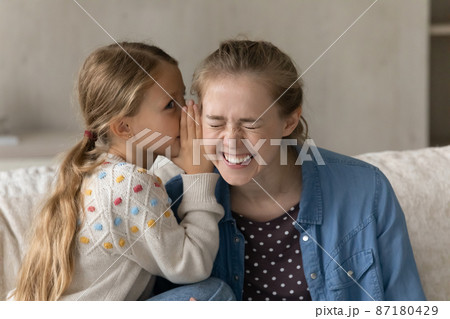 Cute kid telling secret to happy laughing elder sister, nanny Cute kid telling secret to happy laughing elder sister, nanny 87180429