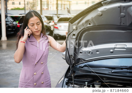 Young Asian woman having a trouble about her car and try to use a smartphone to call an assistant for help or advise. Asian woman asking for an emergency service due to car accident. Young Asian woman having a trouble about her car and try to use a smartphone to call an assistant for help or advise. Asian woman asking for an emergency service due to car accident. 87184660