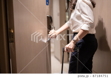 Unrecognizable businesswoman in smart casual carrying a hard suitcase to the room in hotel and using room keycard to unlock the door. 87184751