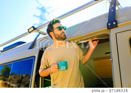 man in charming trailer house makes coffee outdoors in mountains in summer sunny day 87186328