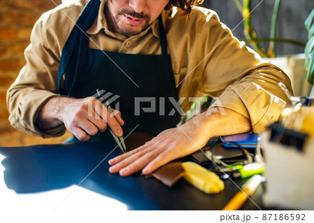 hobby became a small business leather man in apron is making a leather wallet and shooes in studio 87186592