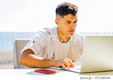 Happy argentinian student sinning with laptop outdoors and looking glad 87186694