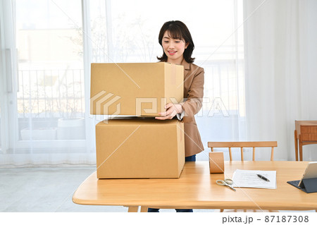 机の上の段ボールを二つ重ねて持ち上げる女性 87187308