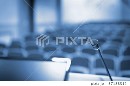 Rostrum with microphone and computer in conference hall, blue toned Rostrum with microphone and computer in conference hall, blue toned 87188312