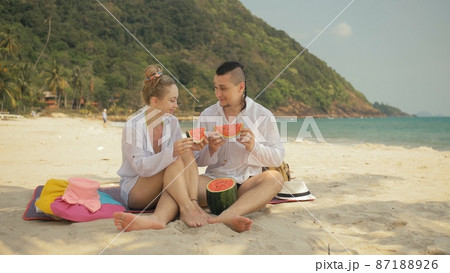 The cheerful love couple holding and eating slices of watermelon on tropical sand beach sea. Romantic lovers two people spend summer weekend. The cheerful love couple holding and eating slices of watermelon on tropical sand beach sea. Romantic lovers two people spend summer weekend. 87188926
