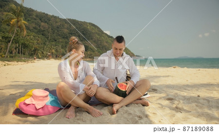 The cheerful love couple holding and eating slices of watermelon on tropical sand beach sea. Romantic lovers two people spend summer weekend. The cheerful love couple holding and eating slices of watermelon on tropical sand beach sea. Romantic lovers two people spend summer weekend. 87189088